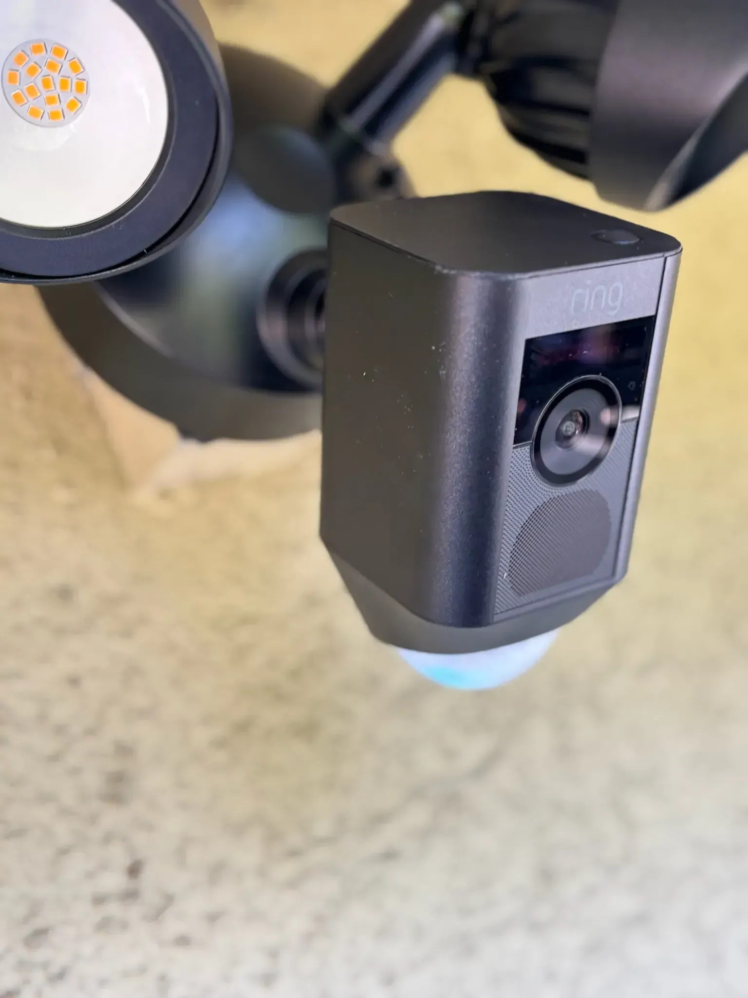 A black Ring security camera with an integrated floodlight mounted on a light-colored surface.