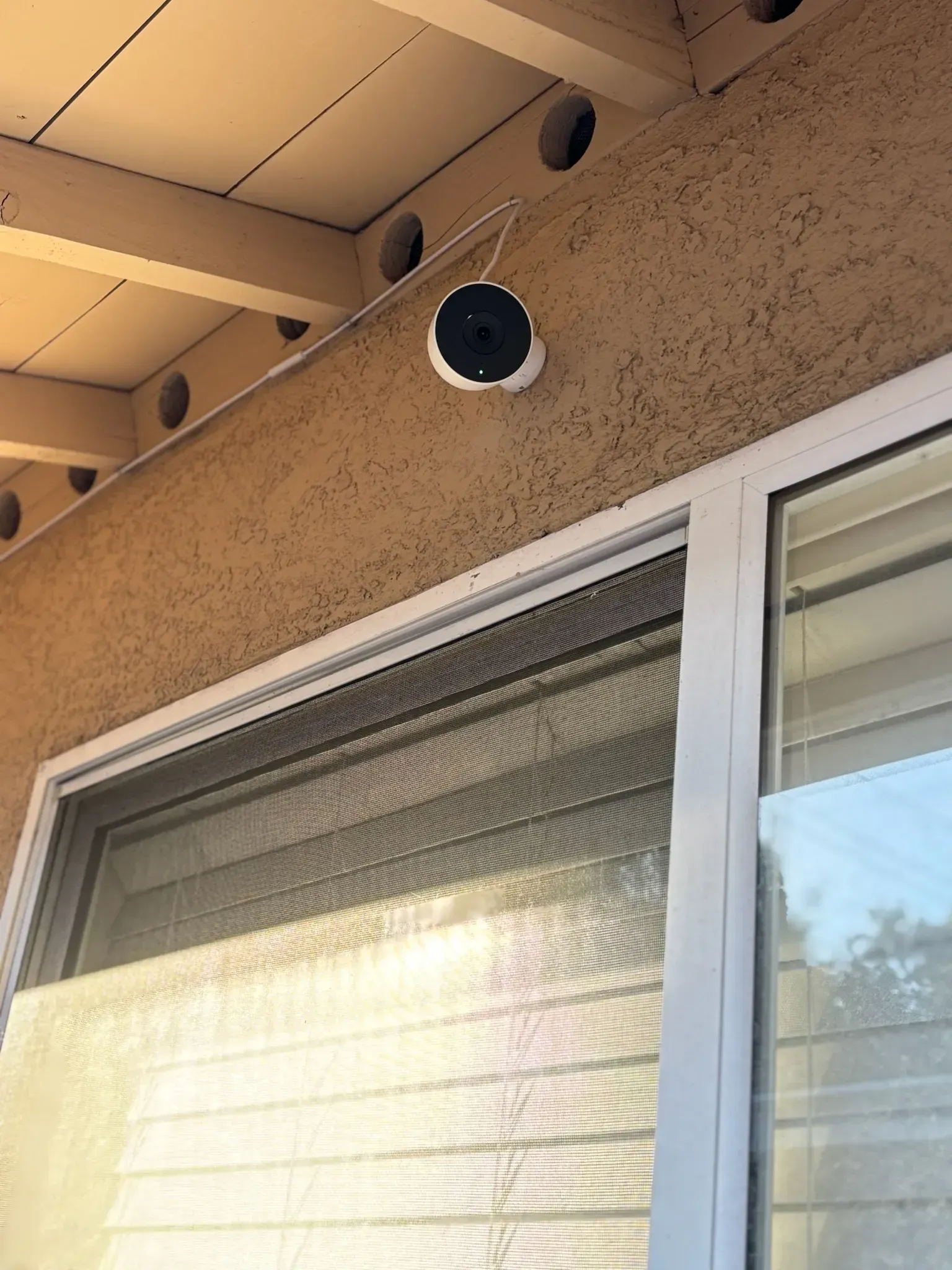 A white circular security camera mounted on a textured beige exterior wall above a window.