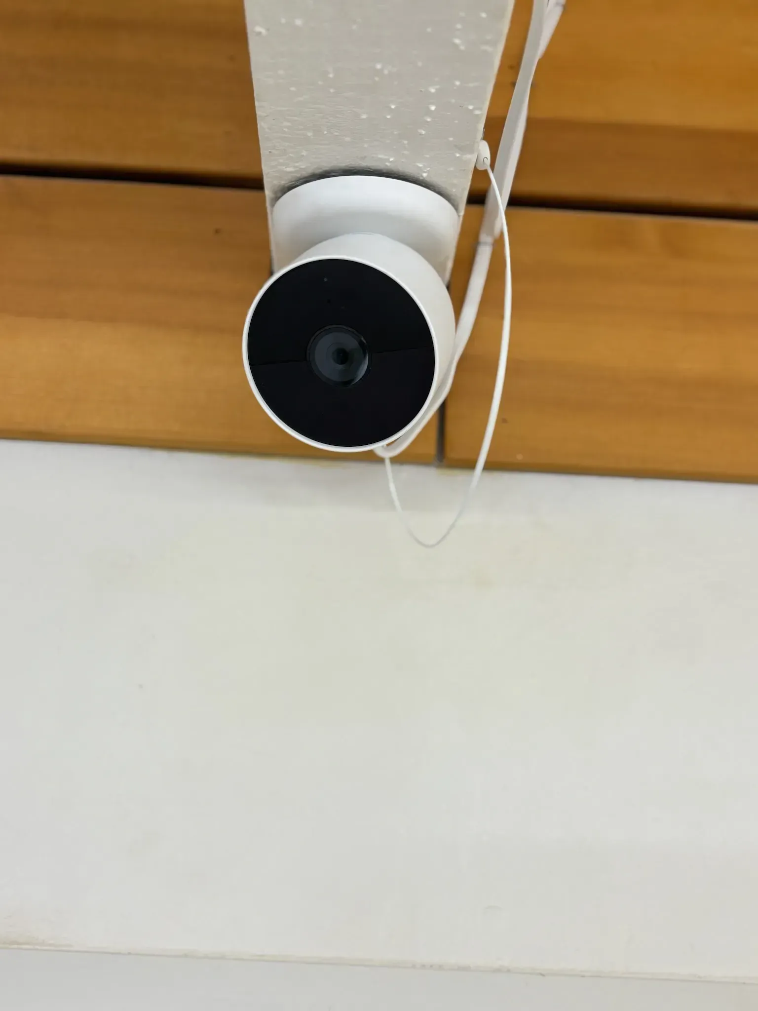 A white security camera mounted on a wall against a wooden background.