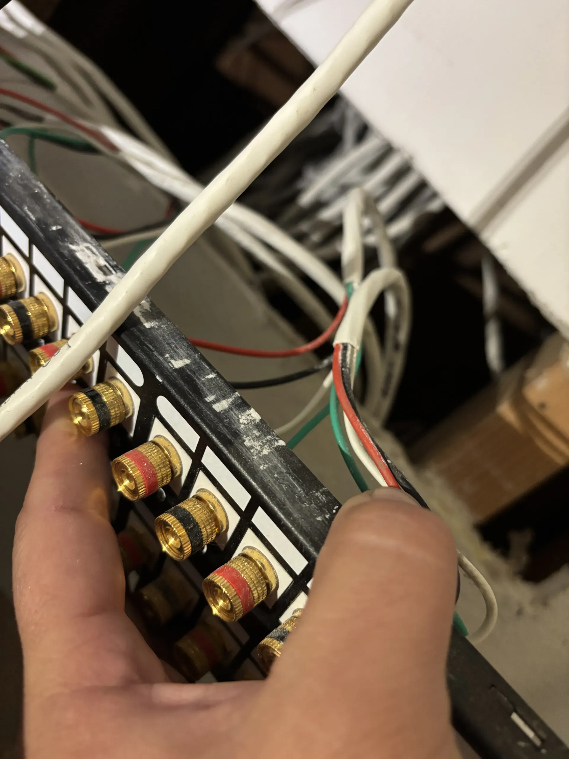 A hand holds a speaker wire terminal block with multiple gold-plated connectors and various colored wires attached.