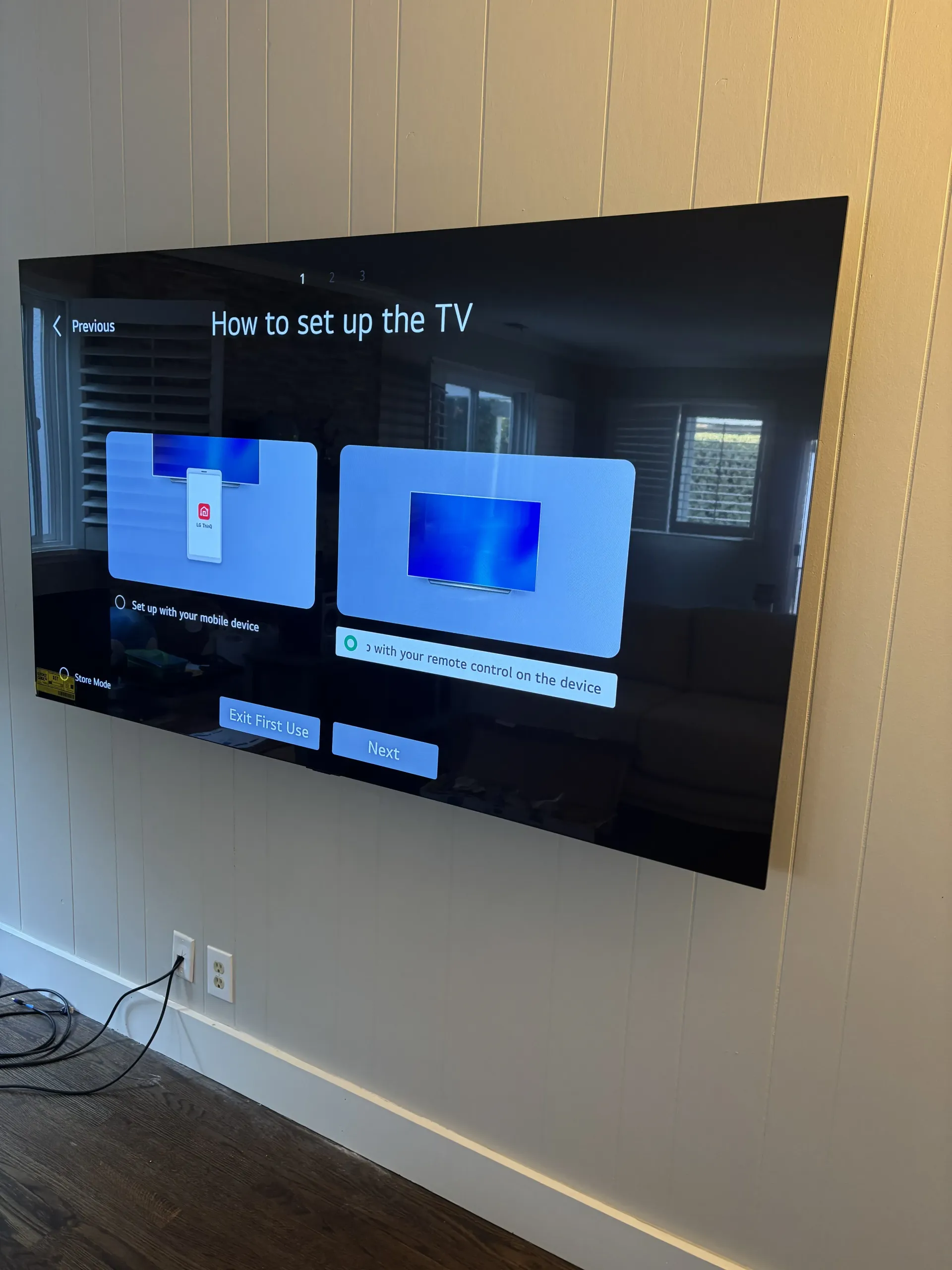 A wall-mounted television displays a setup menu with two options, in a room with dark flooring and light walls.