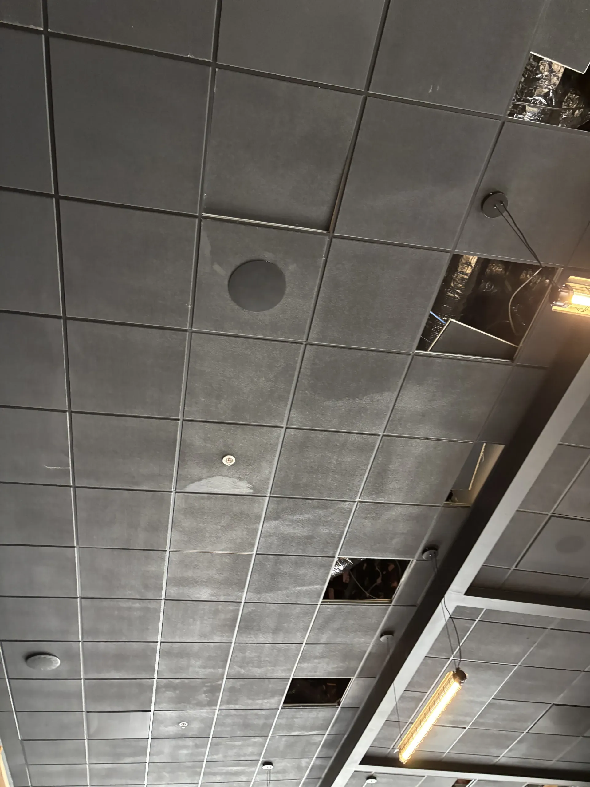 A dark gray drop ceiling grid featuring several missing tiles, exposing the mechanical space and wiring above.