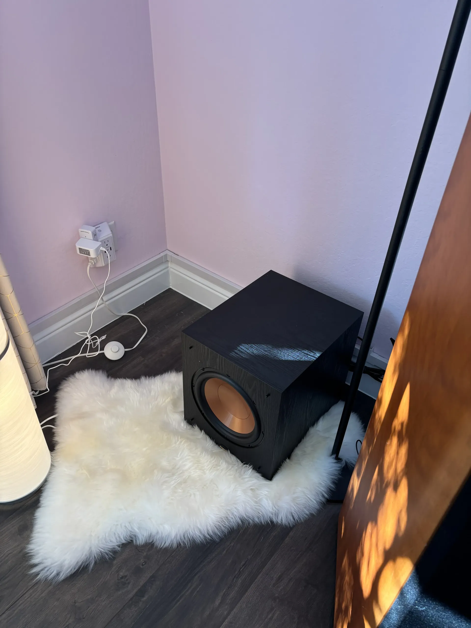 A Klipsch subwoofer with a copper-colored driver sits on a white faux fur rug in the corner of a room with pink walls.
