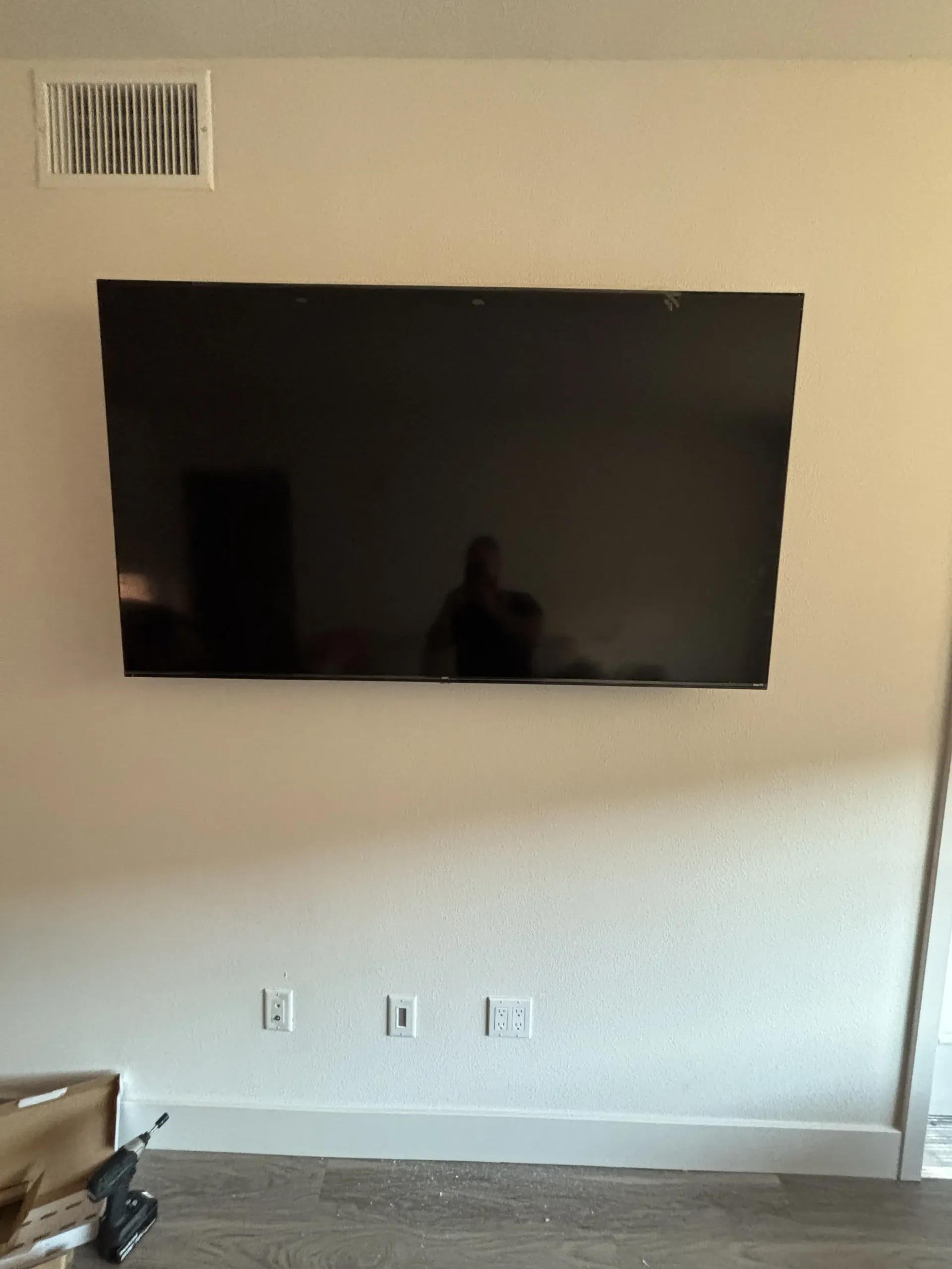 A large, black flat-screen television mounted on a plain, light-colored wall above three electrical outlets.
