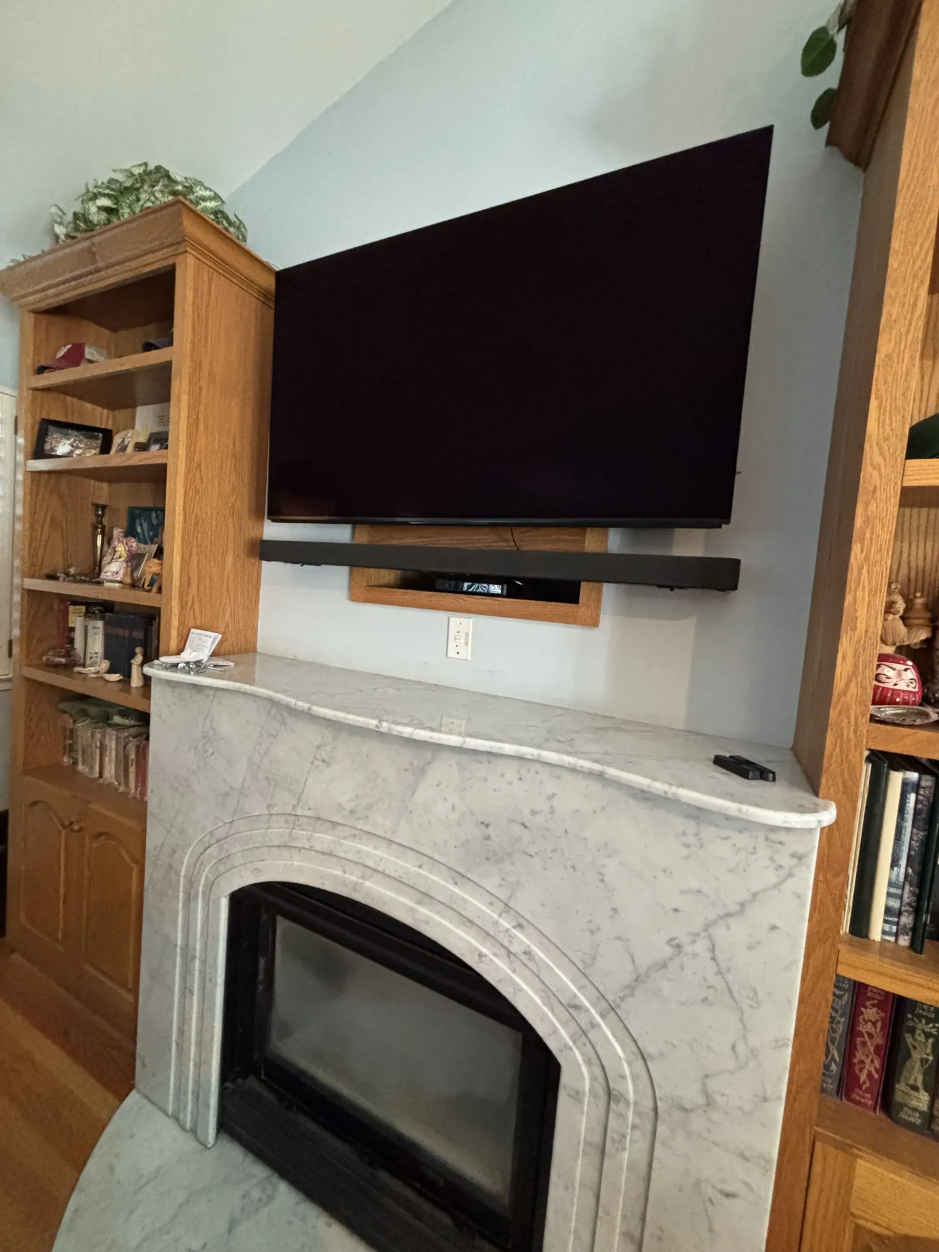 A television and soundbar mounted above a light grey marble fireplace, flanked by tall wooden bookshelves.