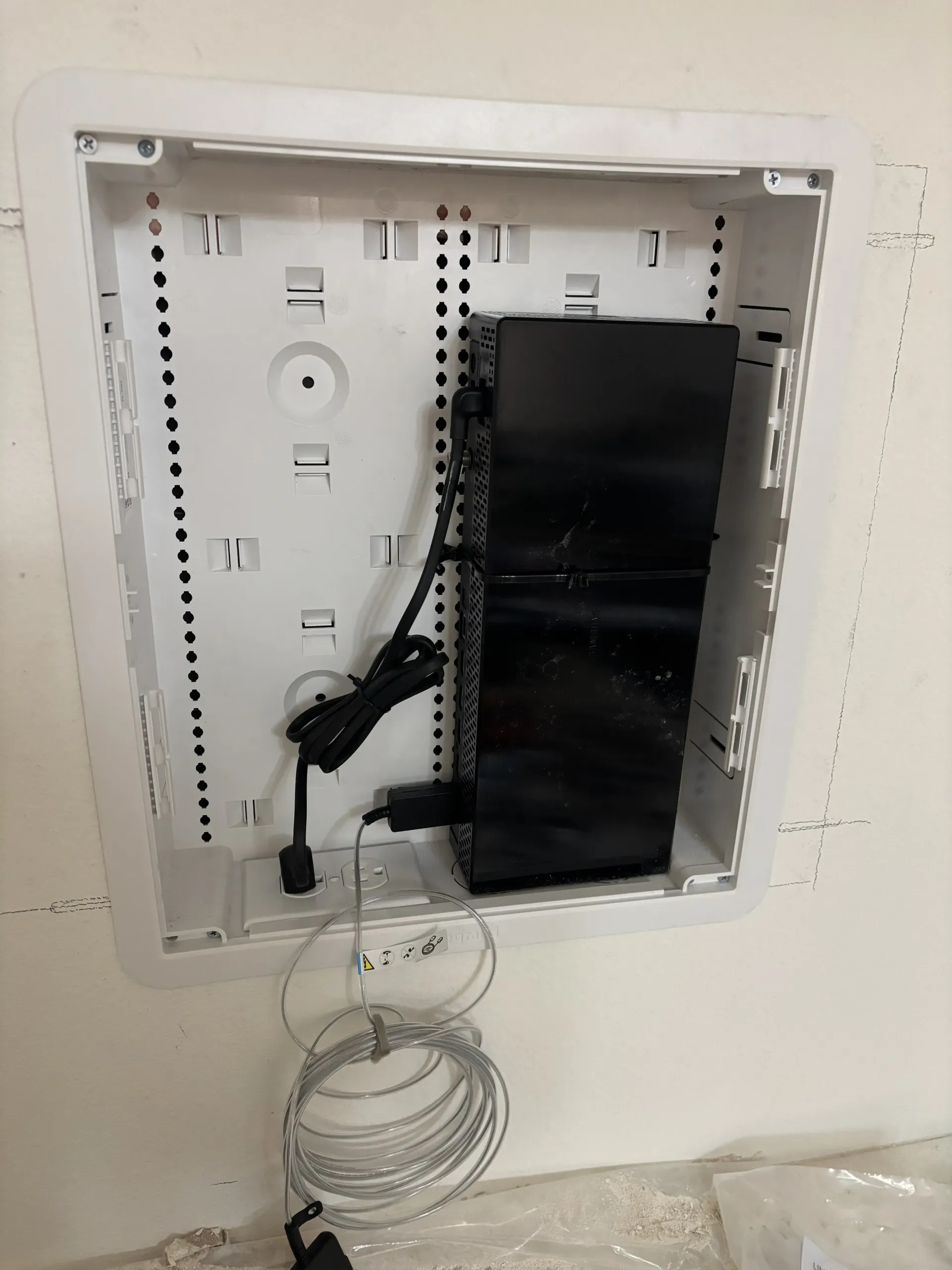 A white wall-mounted media enclosure containing a black rectangular device and coiled white cables.