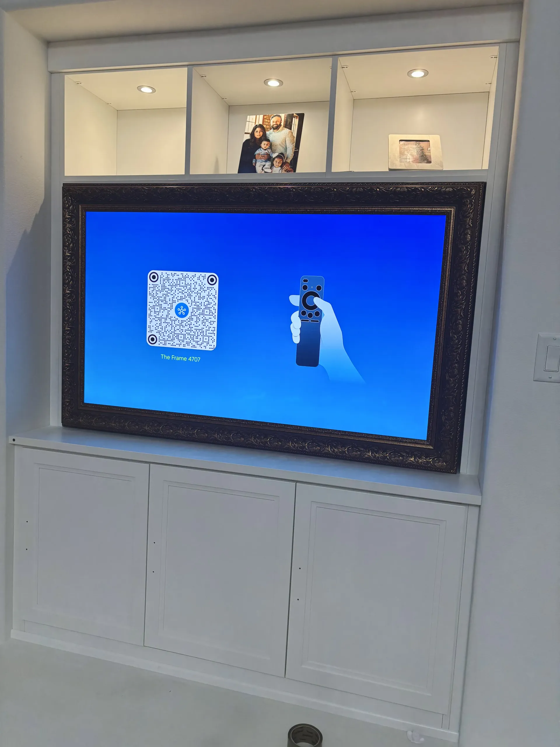 A framed television in a white built-in cabinet displays a QR code and a remote control icon on a blue screen.