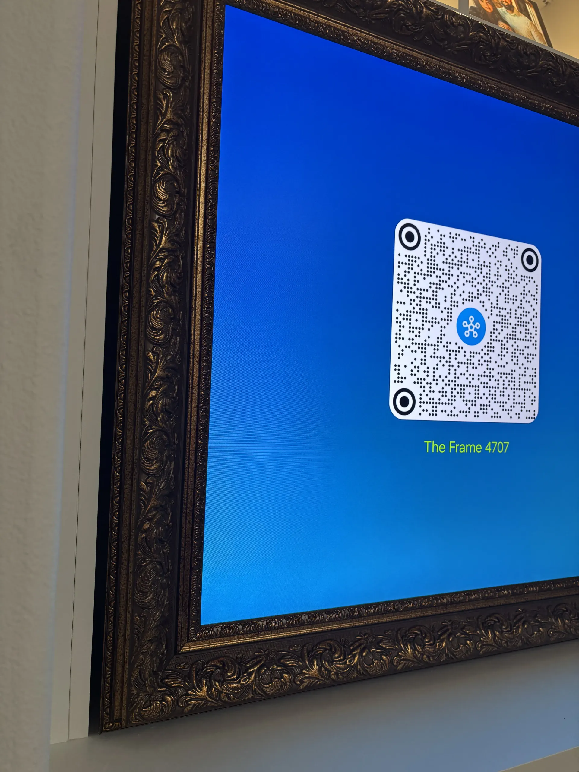 A framed digital display on a wall showing a QR code on a blue background with the text 