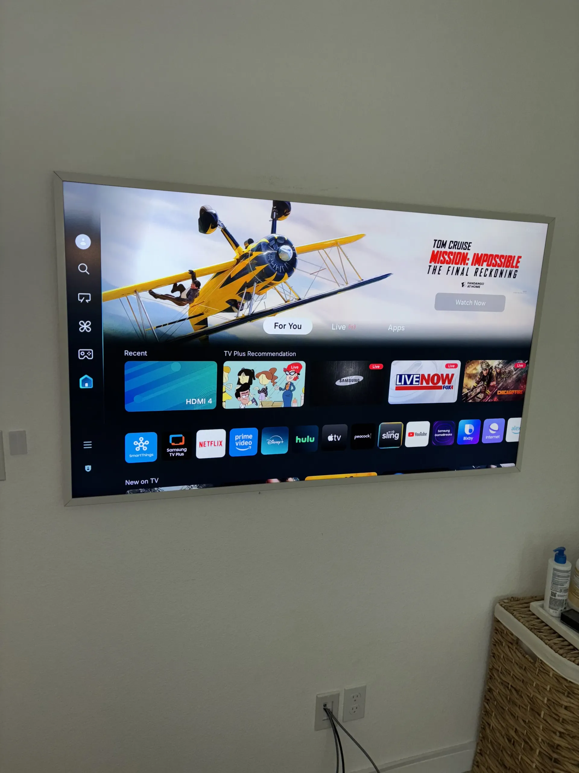 A wall-mounted smart TV displaying a home screen with app icons and a featured image of a yellow biplane.