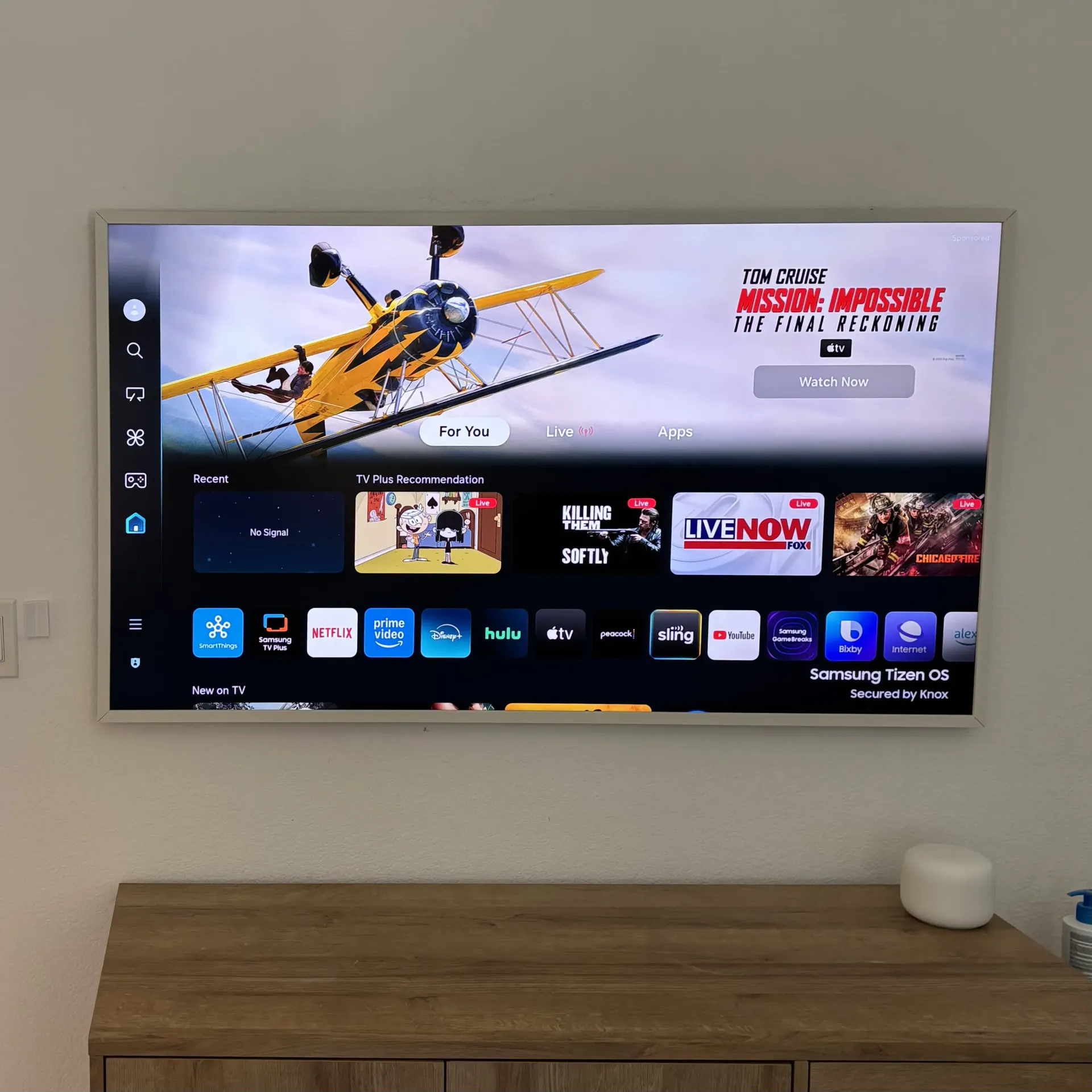A wall-mounted TV displays a smart menu interface featuring a yellow airplane banner and various streaming app icons.