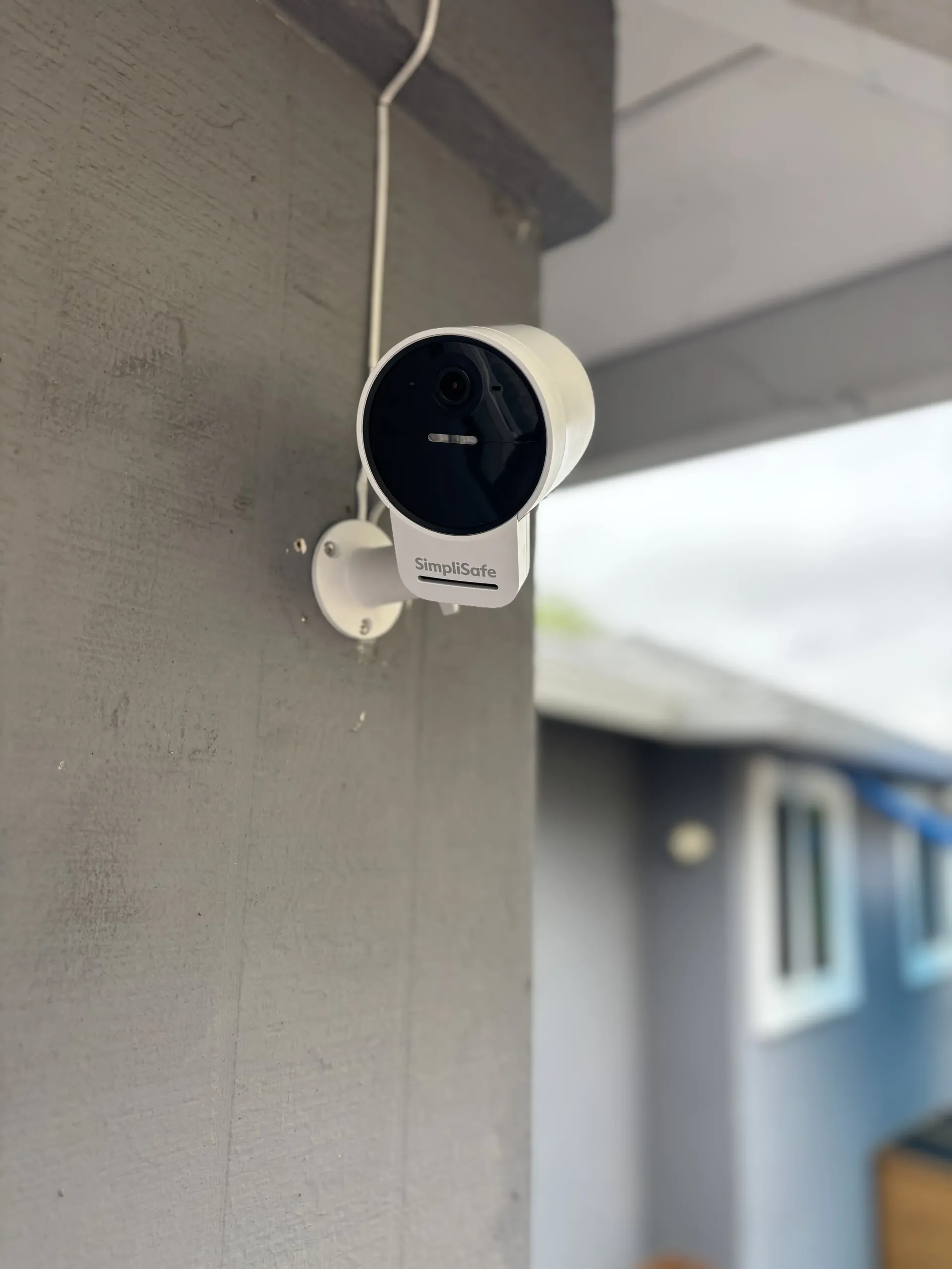 A white security camera mounted to a grey concrete pillar on a porch.