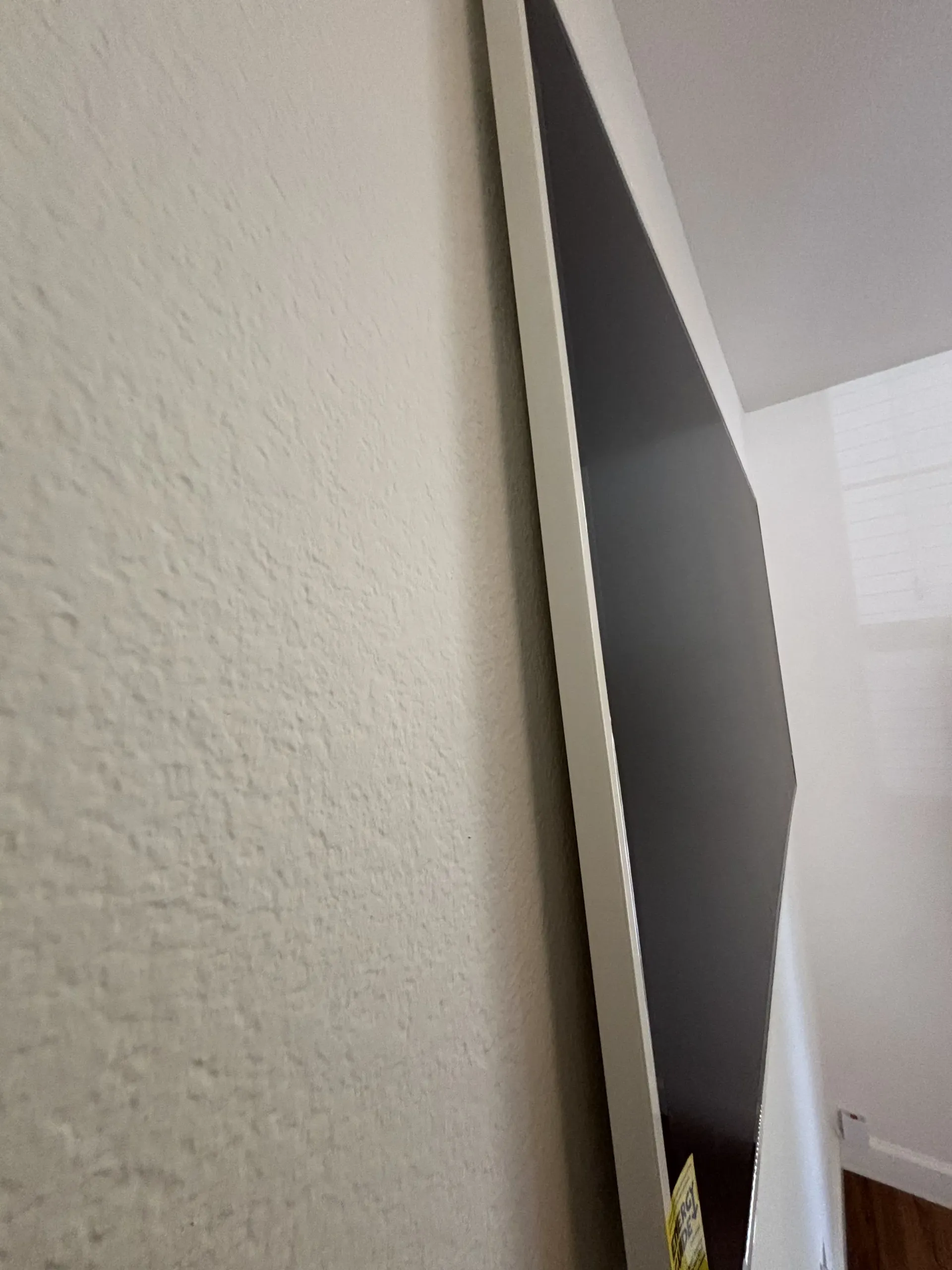 A side view of a flat-screen television with a white frame mounted on a textured, light-colored wall.