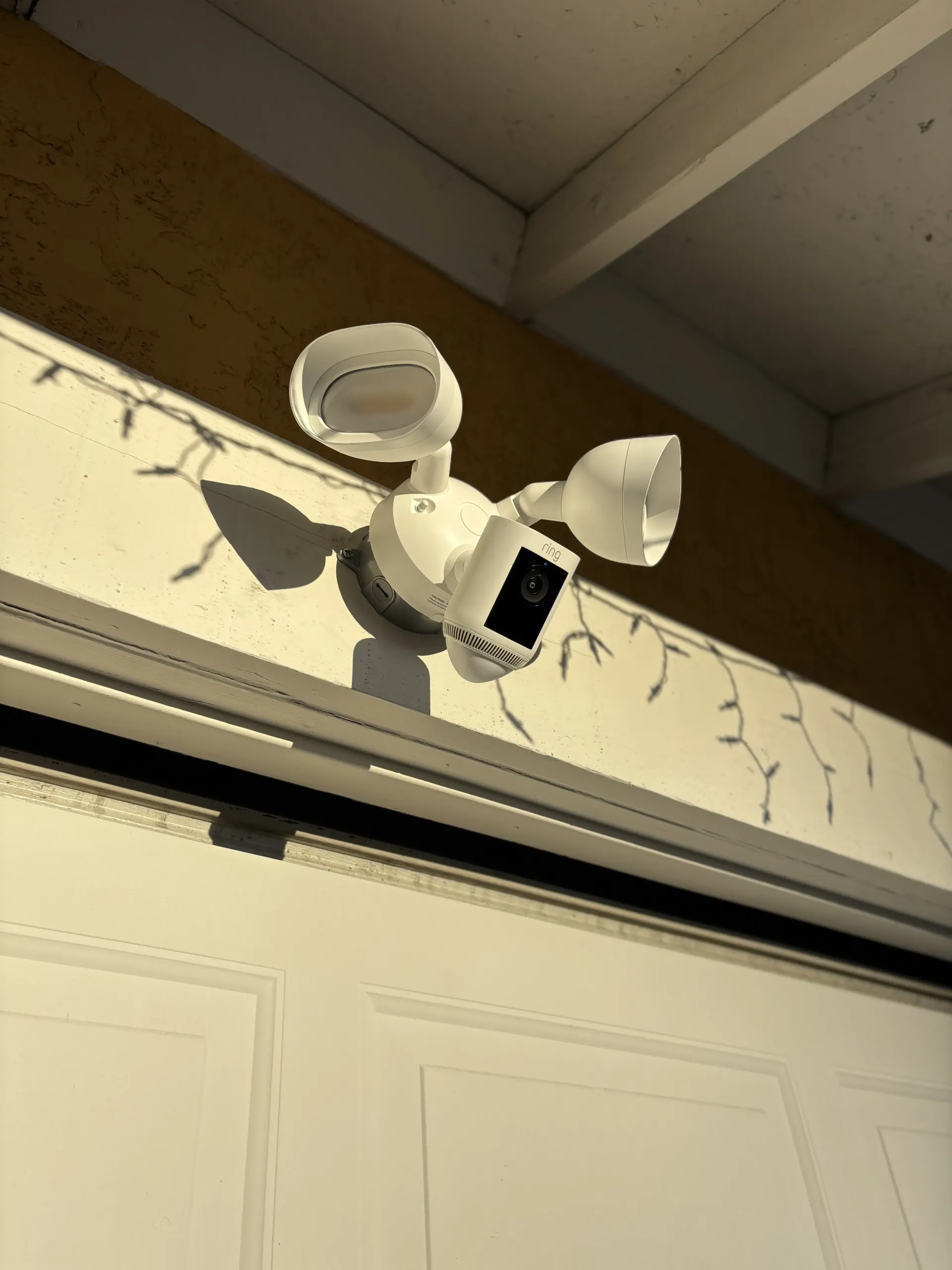 A white Ring floodlight security camera mounted on an exterior wall above a white garage door.