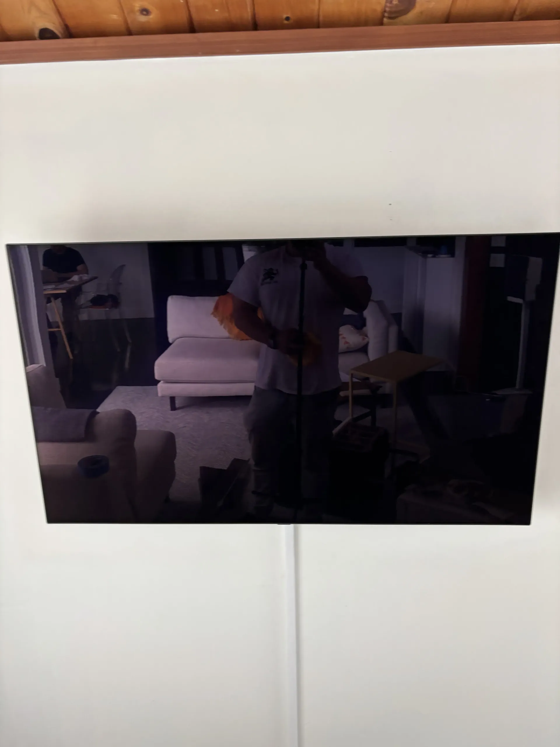 A black television mounted on a white wall, showing a reflection of a living room with furniture.