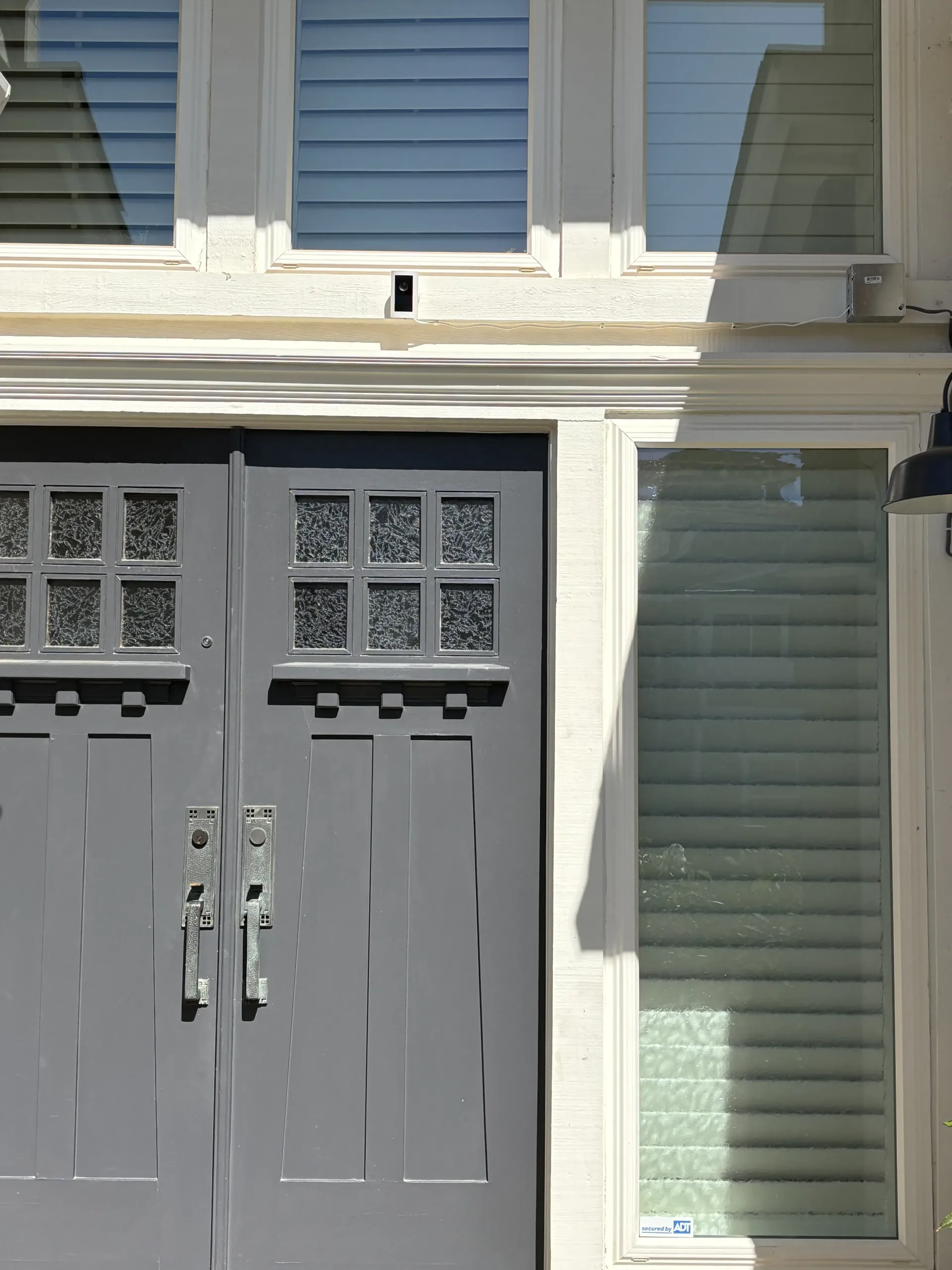 A close-up of a grey double front door with square, textured glass windows above, next to a tall, narrow window.