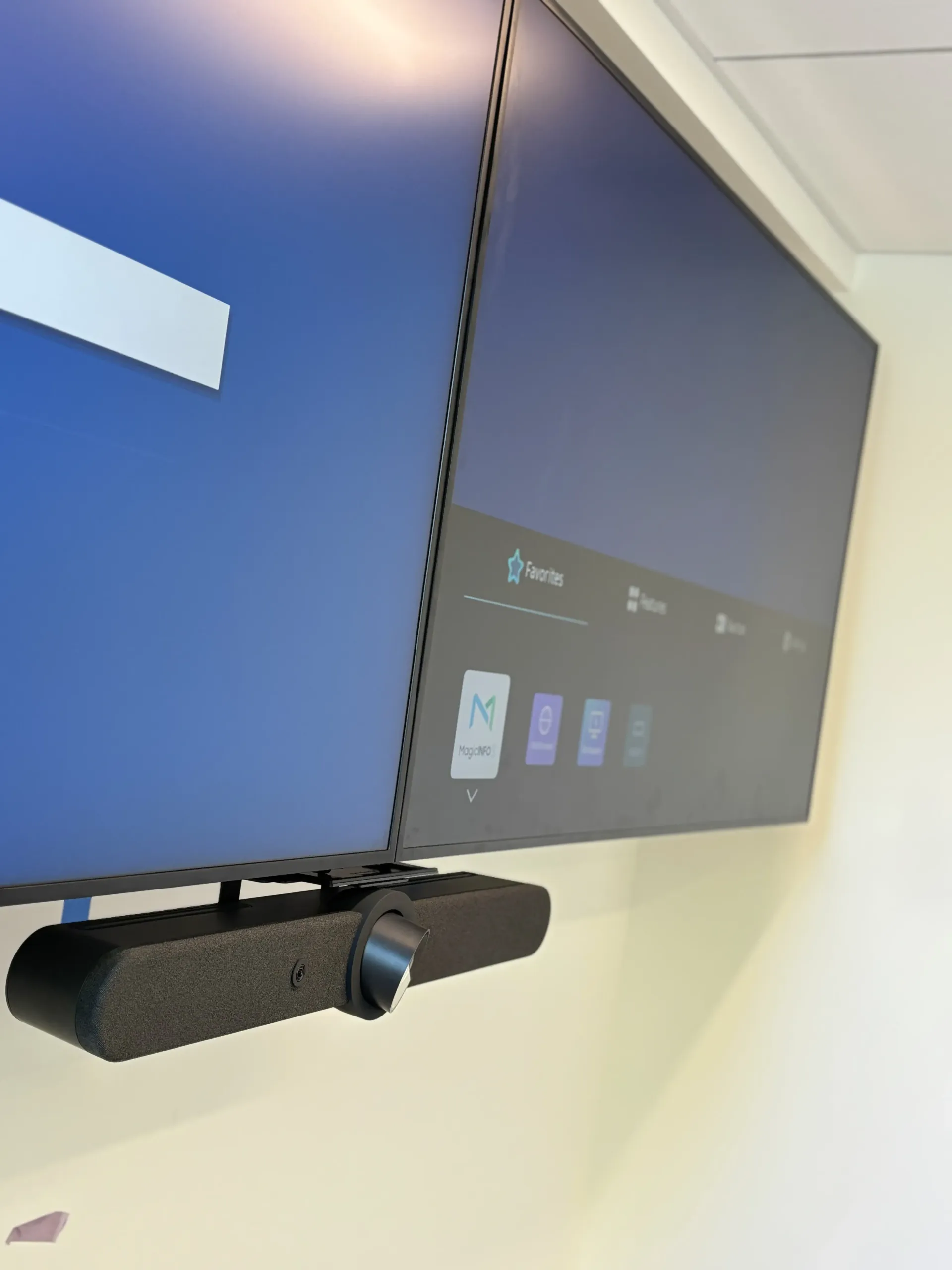 Two monitors mounted on a wall with a video conferencing camera attached underneath the right screen.