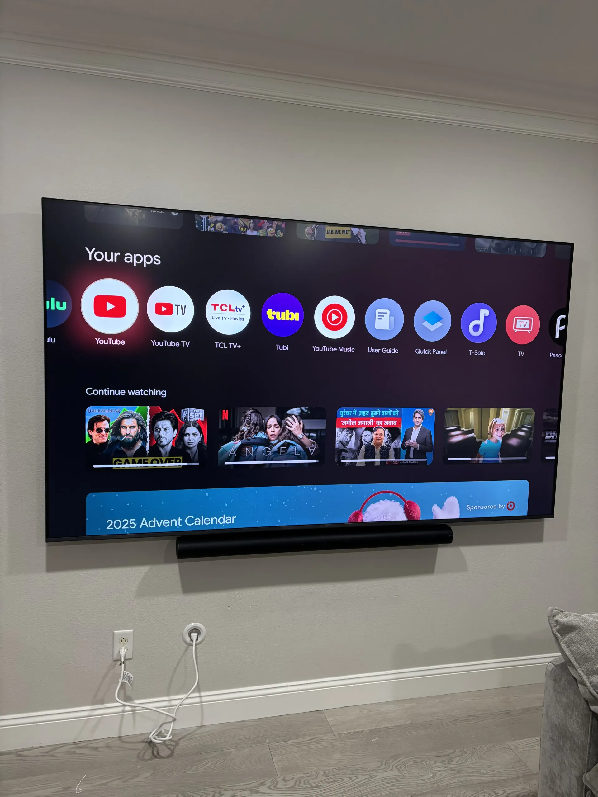 A wall-mounted television displays an Android TV home screen with various streaming app icons and content thumbnails.