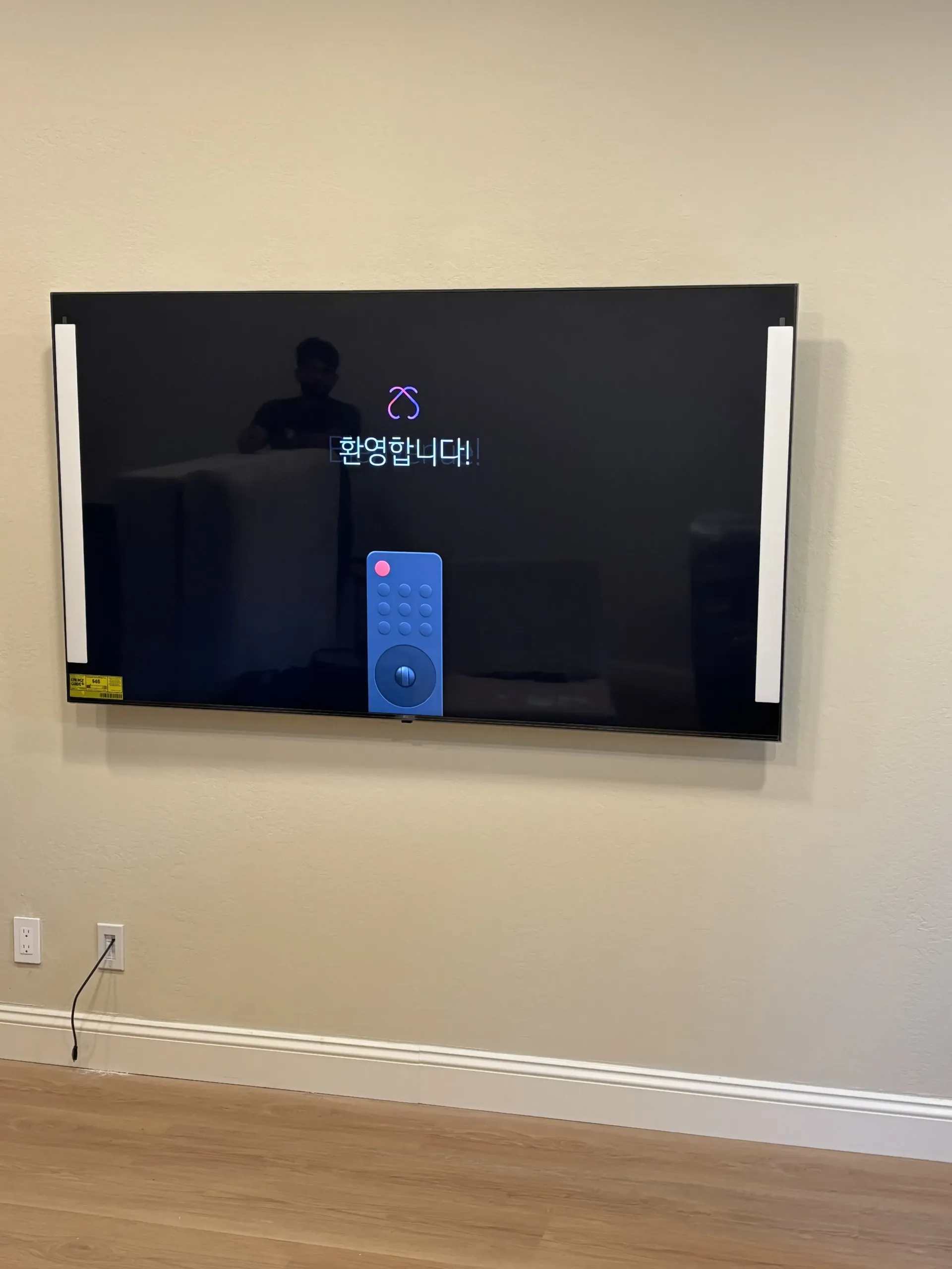A wall-mounted TV showing a remote control icon and Korean text on a dark screen in a room with light beige walls.