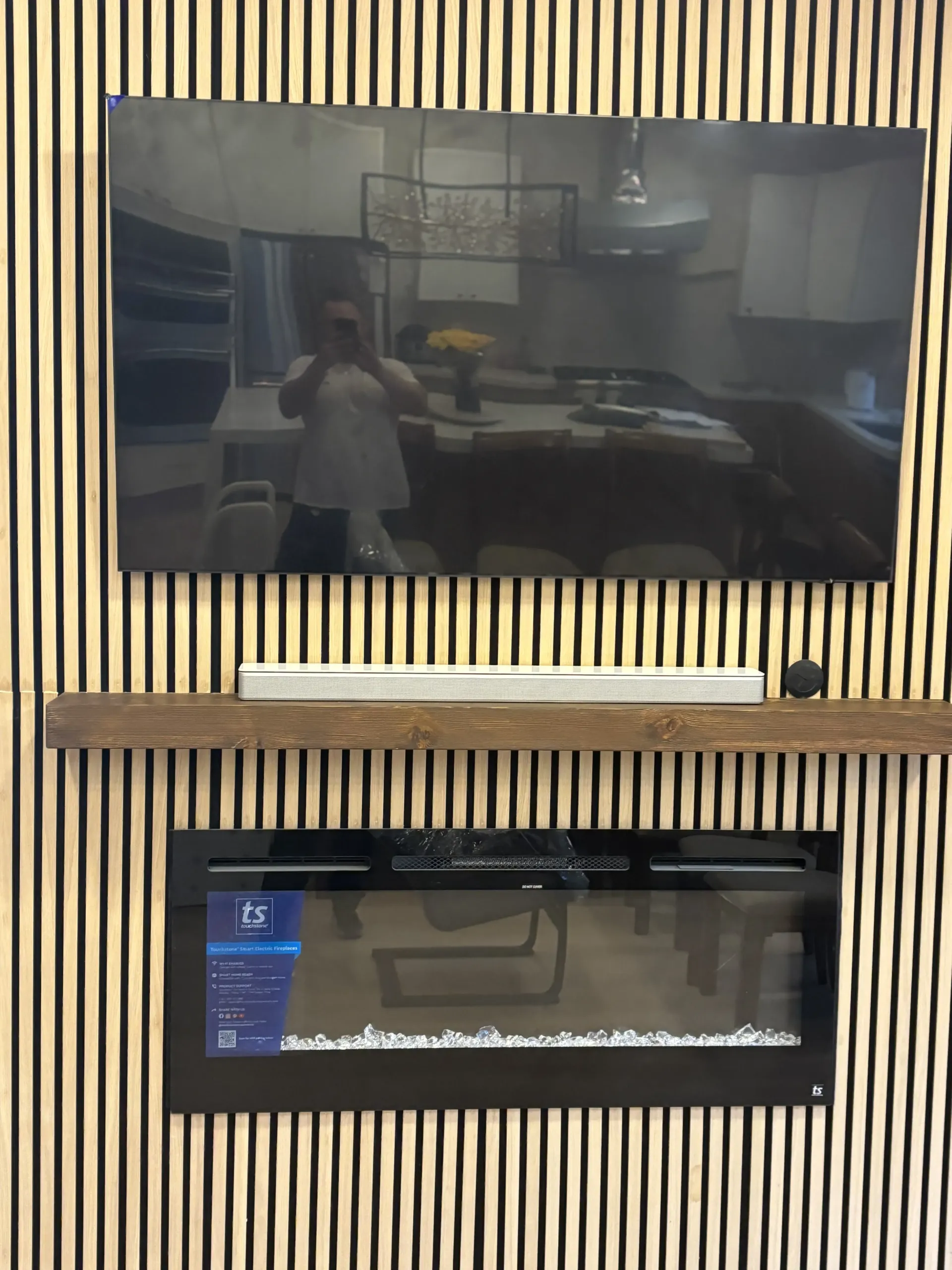 A wall-mounted TV and electric fireplace over a wood mantel, set against a backdrop of vertical wood slat paneling.