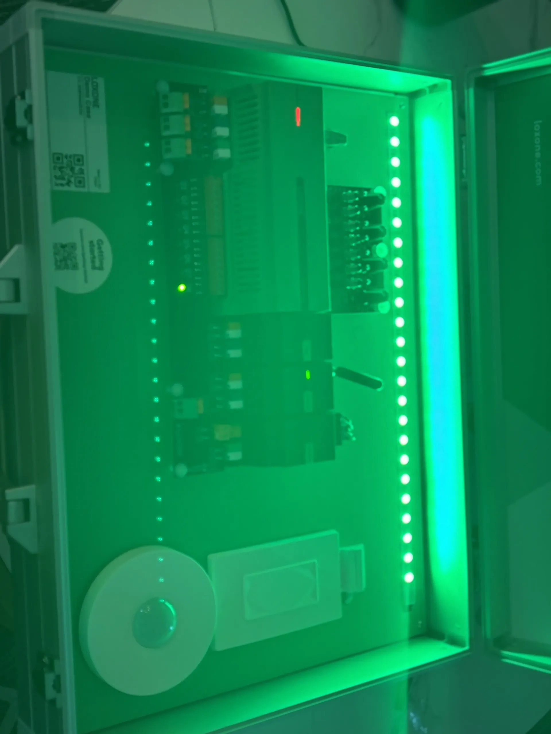 A metal case containing electronic components, circuit boards, and sensors, illuminated by bright green LED strips.