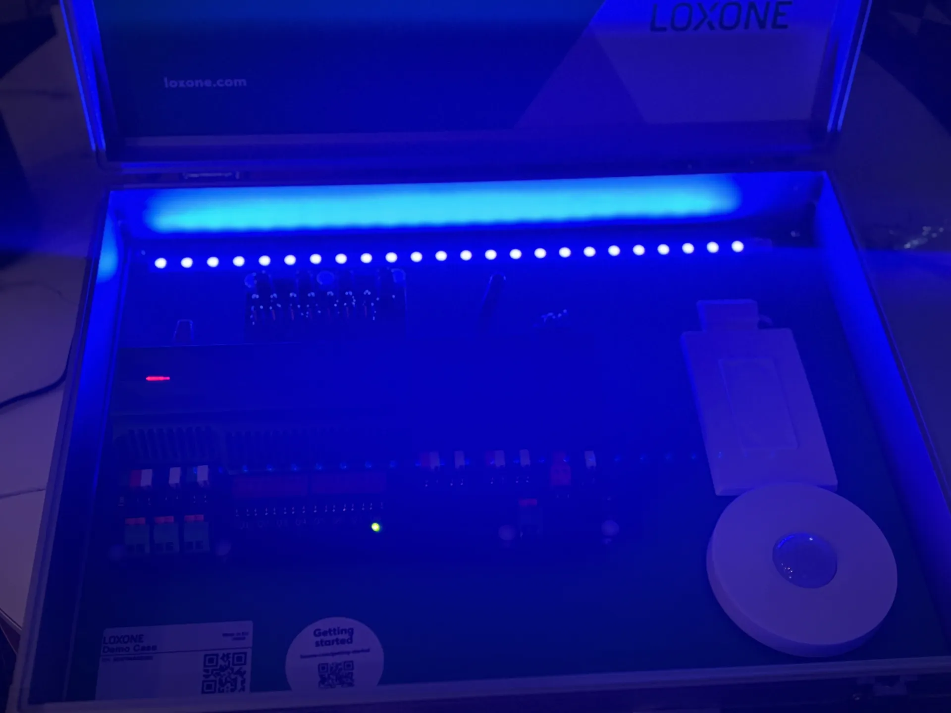 A Loxone demo case open in a dark room, illuminated by blue LED lights, displaying home automation hardware components.