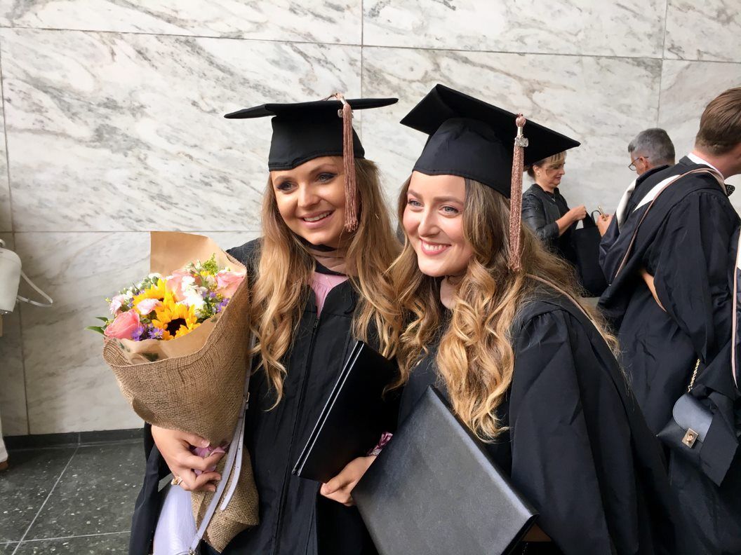 To kvindelige kandidater poserer til et billede, mens de holder en buket blomster.