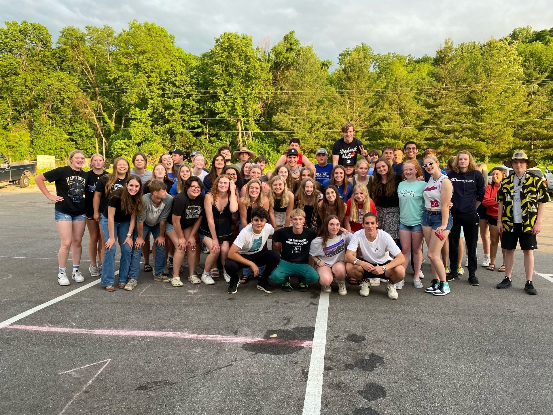 Stor gruppe unge mennesker poserer udenfor; træer i baggrunden.