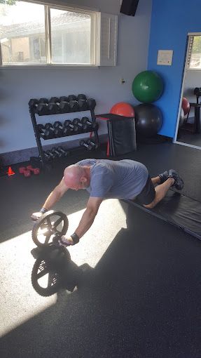 A man is doing push ups on an ab roller in a gym.