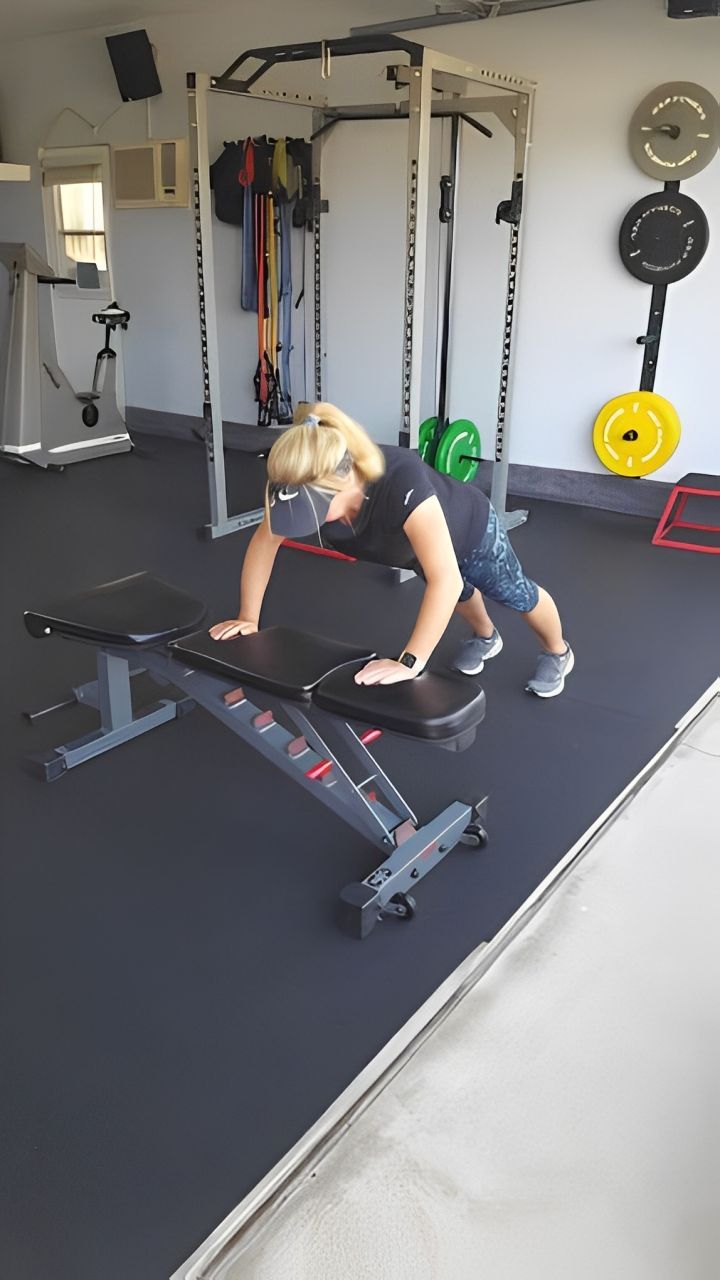 A woman wearing a virtual reality headset is doing push ups on a bench in a gym.