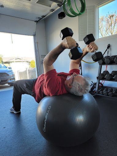 A man is laying on a pilates ball while lifting dumbbells.