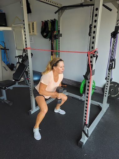 A woman is squatting with a resistance band around her waist in a gym.