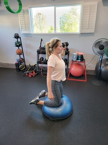 A woman is kneeling on a balance ball in a gym.