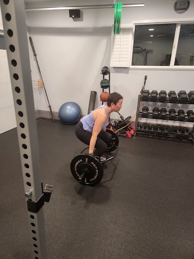 A woman is squatting down with a barbell in a gym.