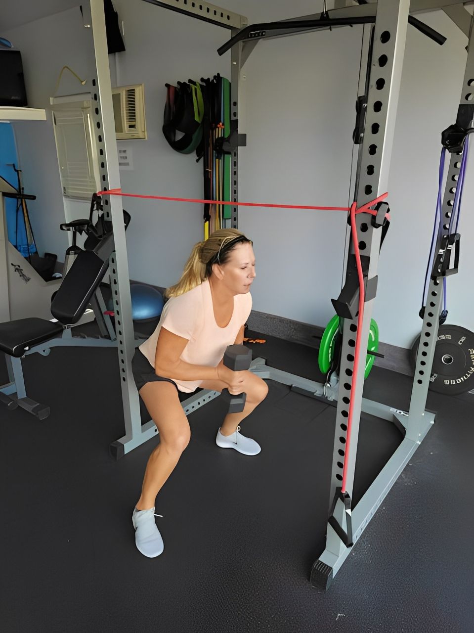 A woman is squatting in a gym with a resistance band around her neck