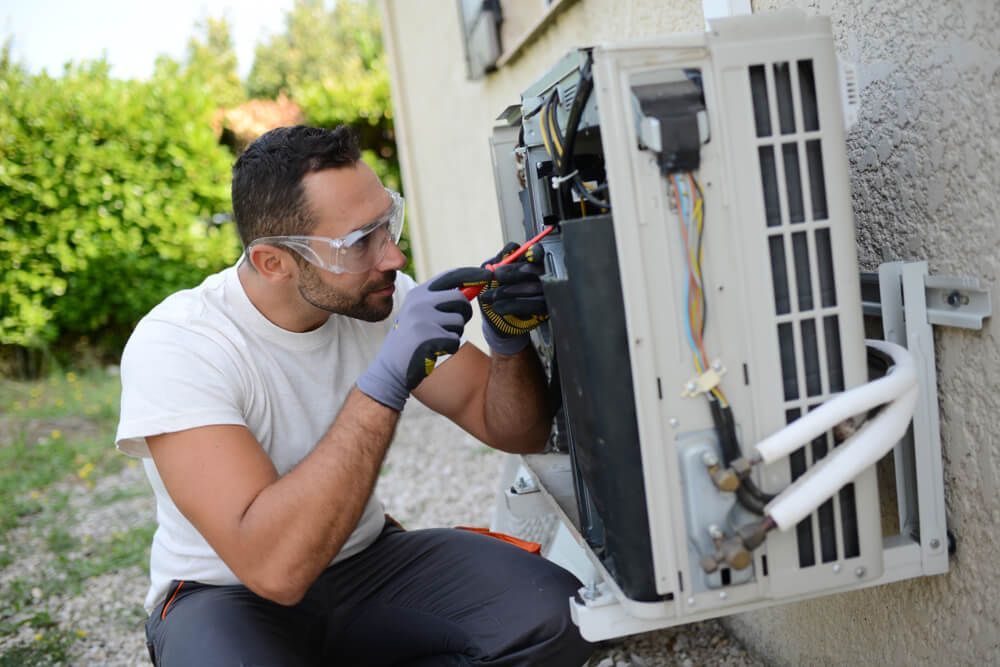 A Man is Working on an Air Conditioner Outside of a Building — DMC Electrical & Air Cooling Pty Ltd in Townsville City, QLD