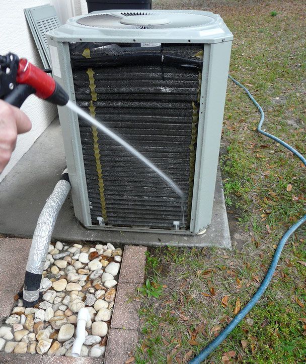 A Person is Cleaning an Air Conditioner With a Hose — DMC Electrical & Air Cooling Pty Ltd in Ayr, QLD