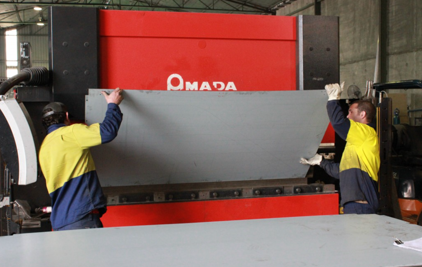 Two Men are Working on a Machine that says Amada on it - DMC Electrical & Air Cooling Pty Ltd in Ayr, QLD