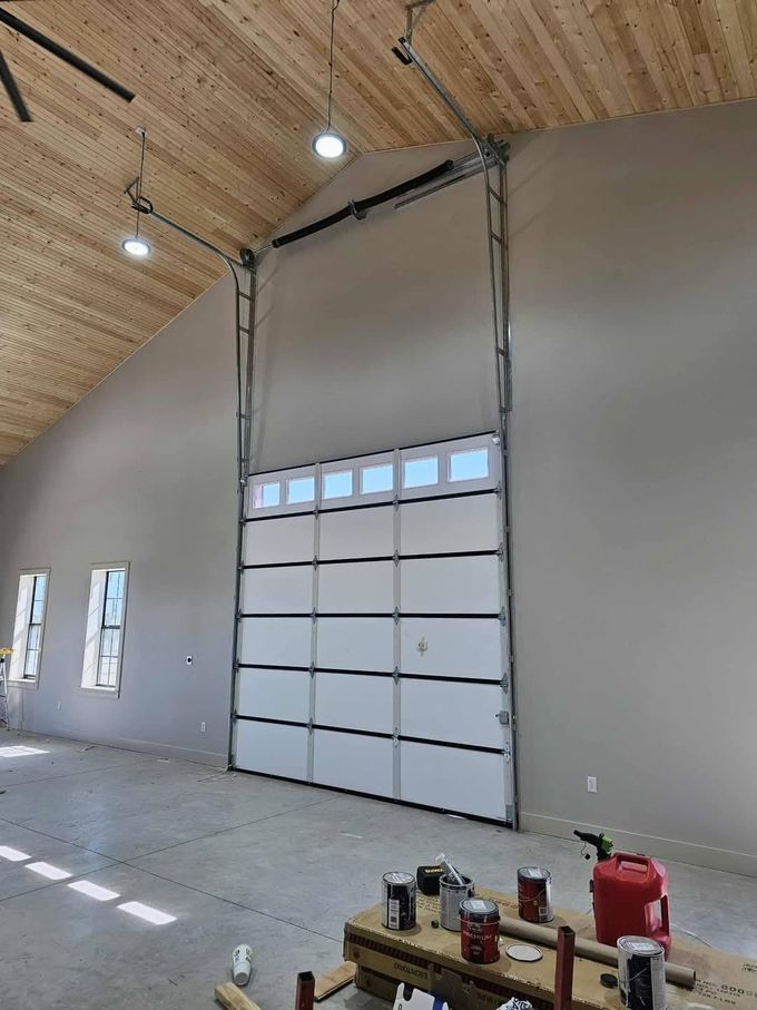 A high-ceiling room with a large, multi-panel garage door featuring a row of windows near the top.
