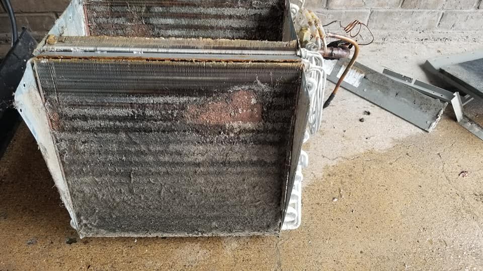 A dirty air conditioner is sitting on the ground next to a brick wall.
