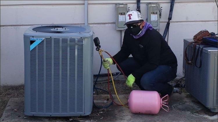A man is working on an air conditioner outside of a building.