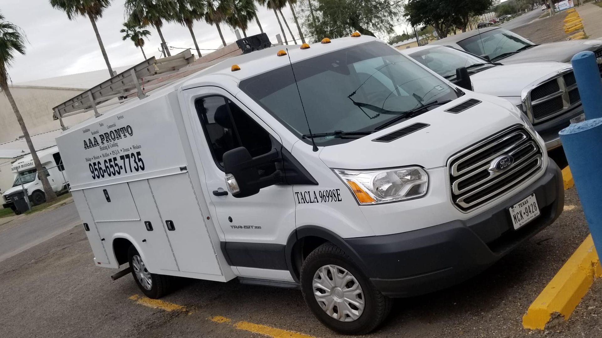 A white van is parked in a parking lot next to a truck.