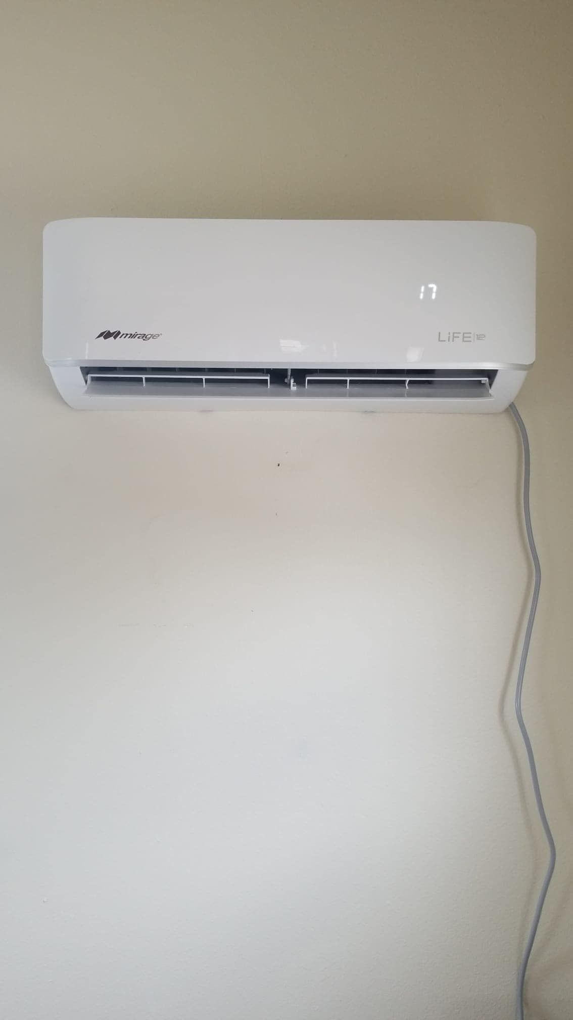 A white air conditioner is hanging on a white wall.
