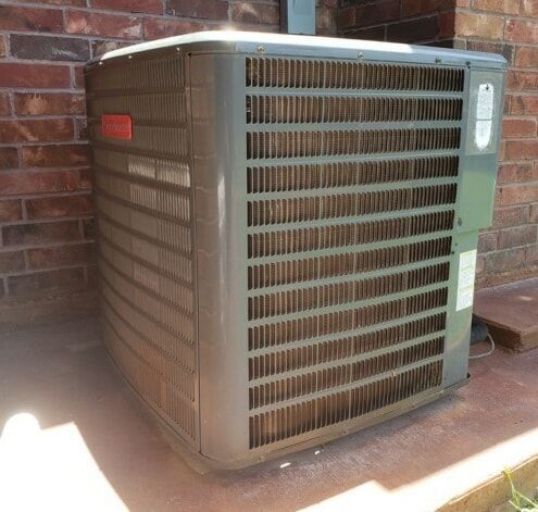 A gray air conditioner is sitting in front of a brick wall