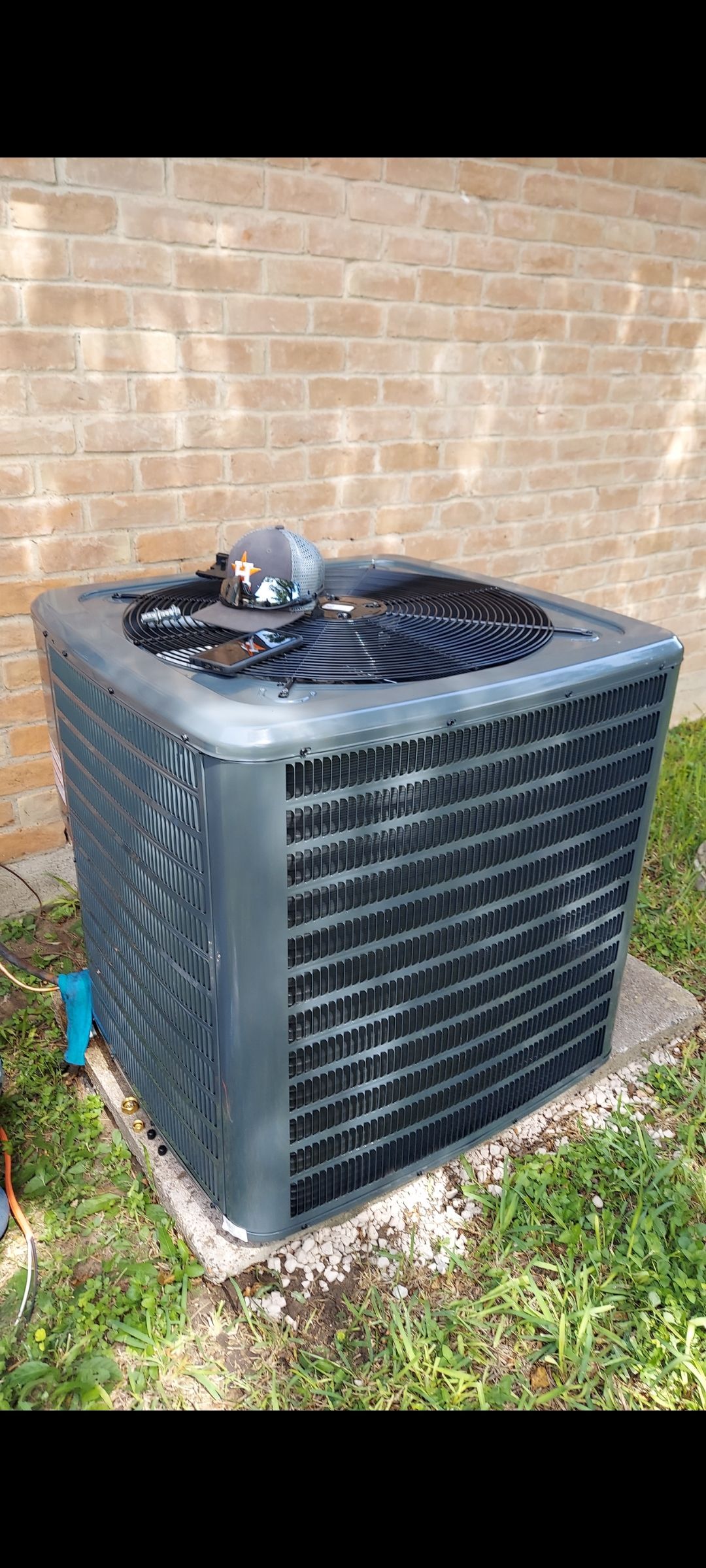 Two men are working on an air conditioner outside of a building.