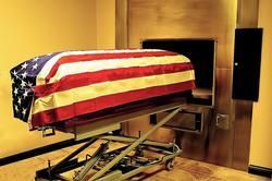 A coffin wrapped in an american flag is sitting on a lift in a room.