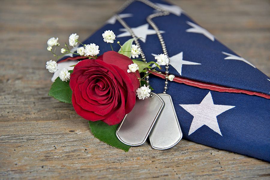 A red rose and dog tags are laying on top of an american flag.