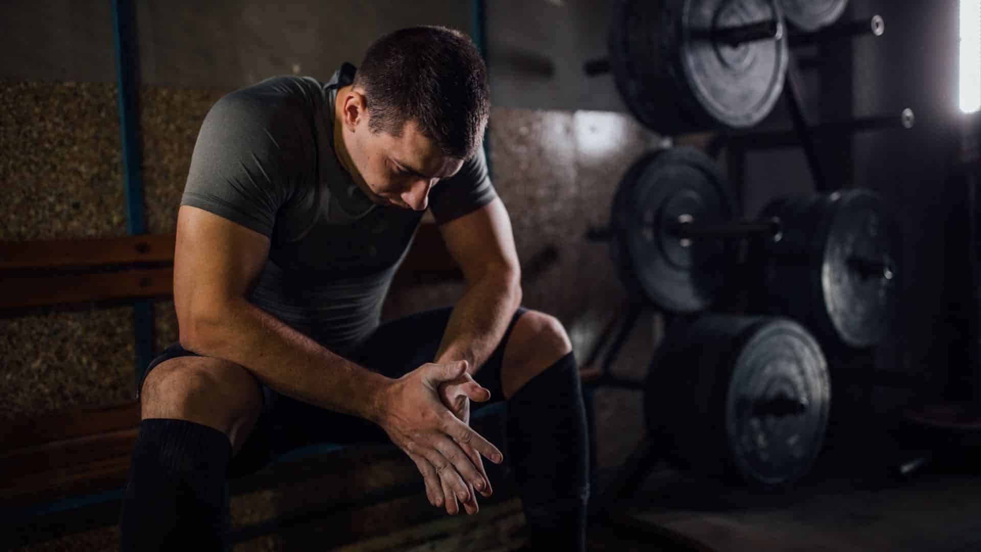 A man is sitting on a bench in a gym with his head down.