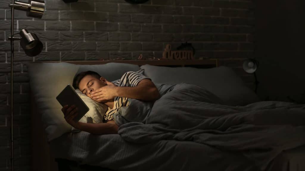 A man is sleeping in bed while reading a book.