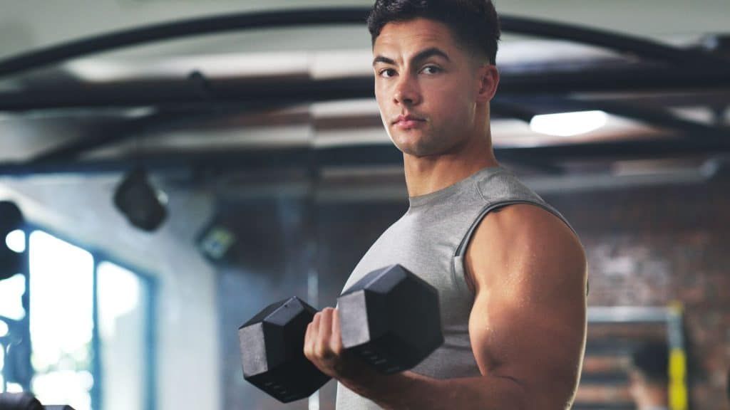 A man is lifting a dumbbell in a gym.