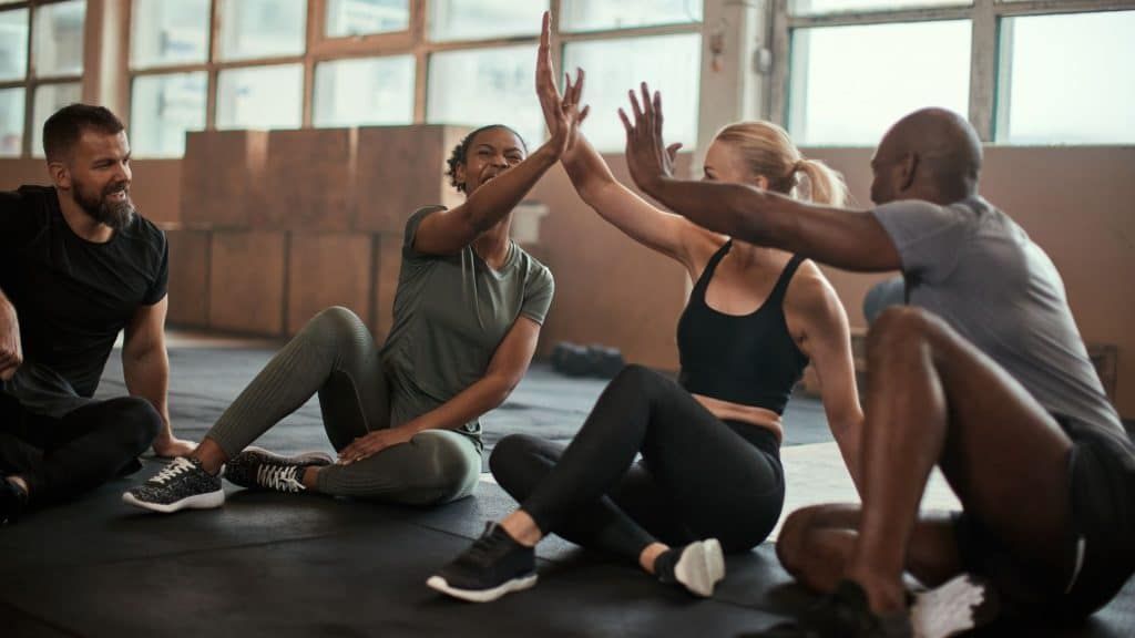 A group of people are giving each other a high five while sitting on the floor in a gym.